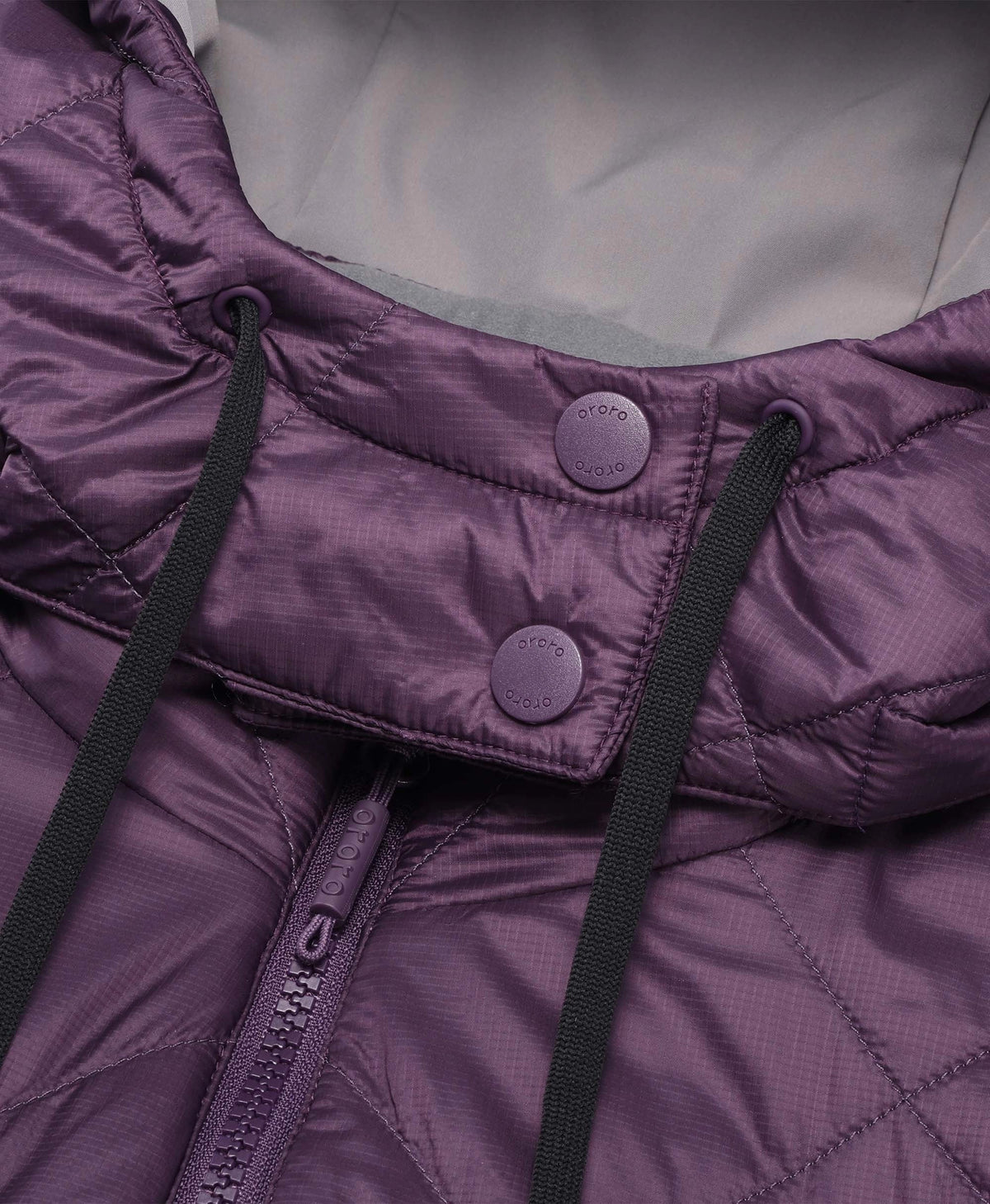 Close-up of a purple quilted puffer jacket showing the collar, snap-button flap, black drawstrings, and a zipper.