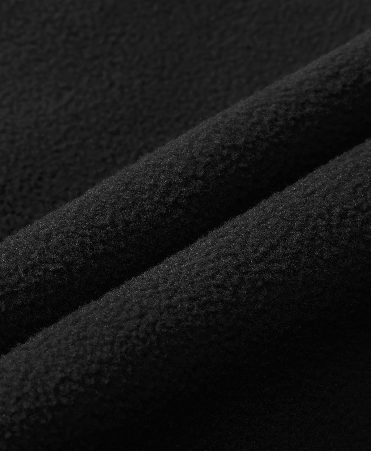 A close-up of black textured fabric with soft diagonal folds showing the material's fine woven texture.