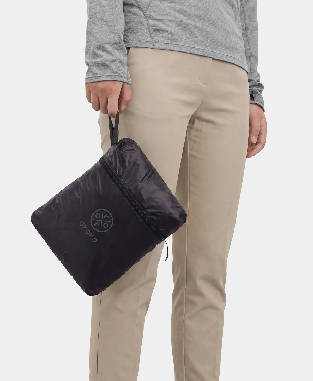 Person holding a black vest packed into its built-in zippered pouch