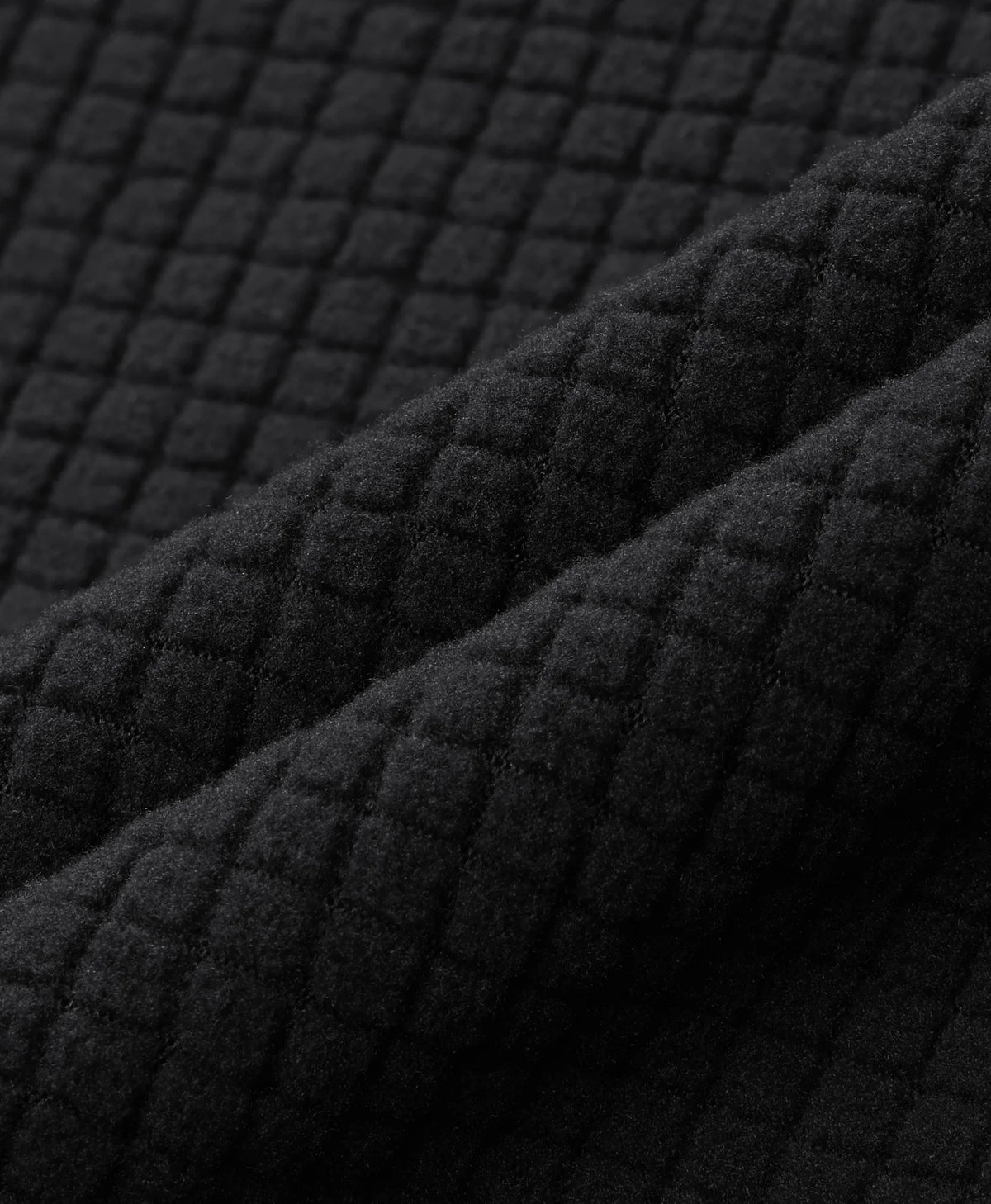 Close-up of a black quilted fabric with a textured diamond pattern, shown in soft folds.