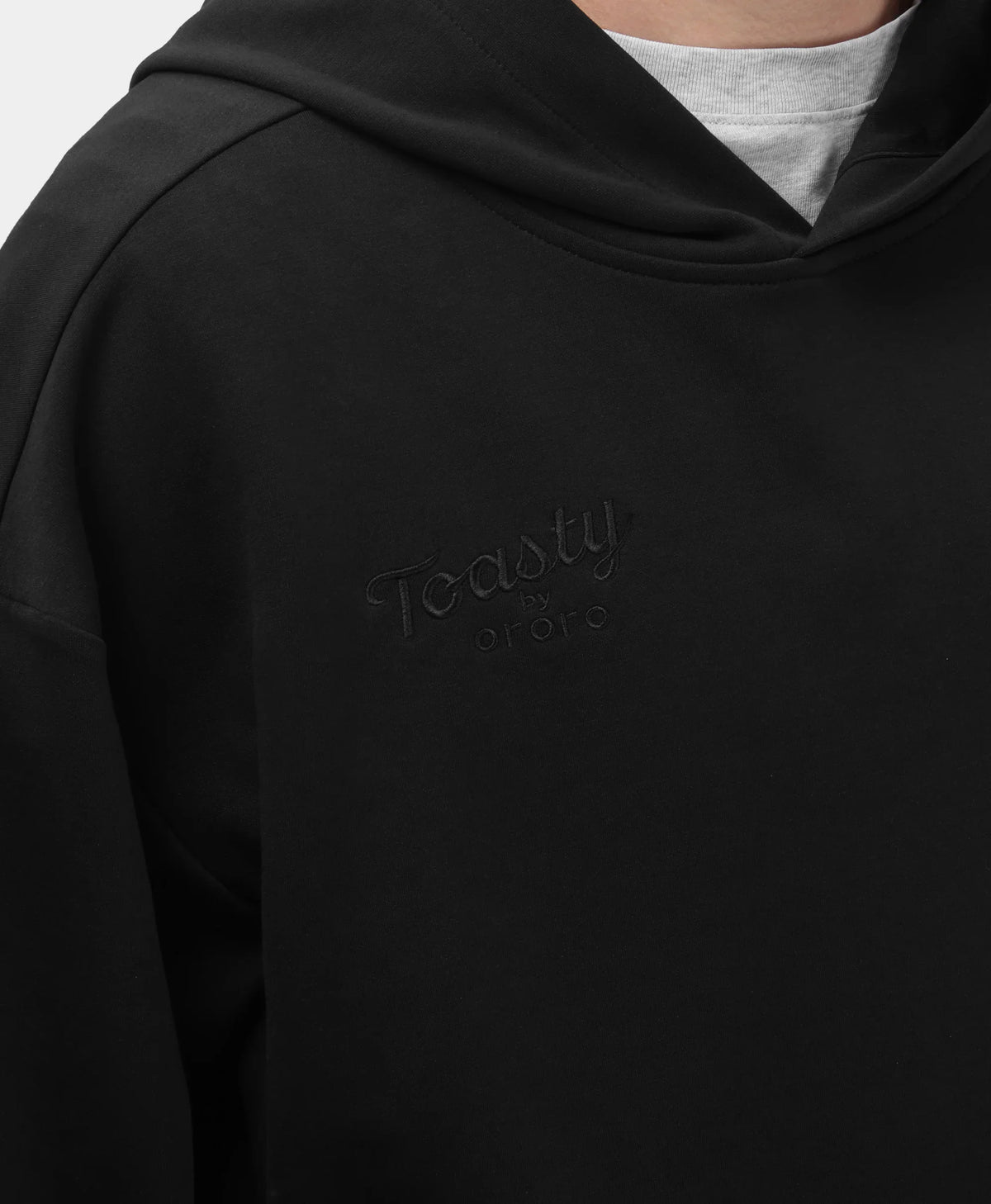 A black Toasty Unisex 5-Zone Heated Pullover Hoodie, featuring a close-up view of the collar area and the subtle tonal embossed "Toasty by ororo" logo on the left chest.