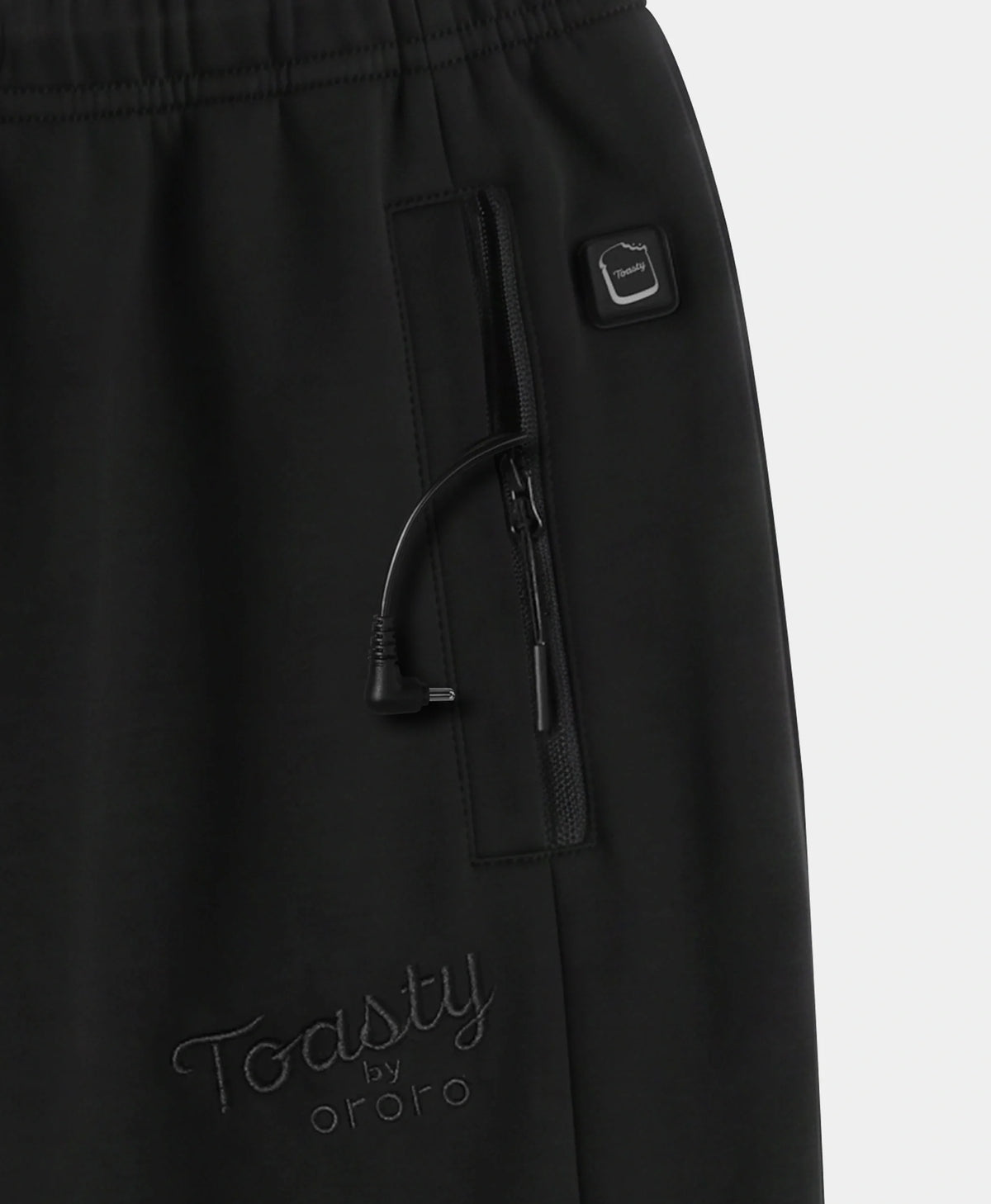 Close-up of black pants showing a side zip pocket with a drawstring, a small square logo tab, and tonal embroidered 'Toasty by ororo' branding near the lower left leg.